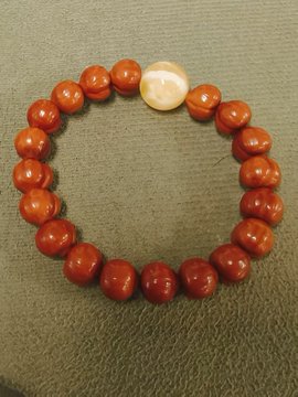 A red beaded bracelet with a single white pearl-like bead displayed on a textured beige surface. The image appears to be a decorative or aesthetic post unrelated to the cryptocurrency trading content mentioned in the caption.