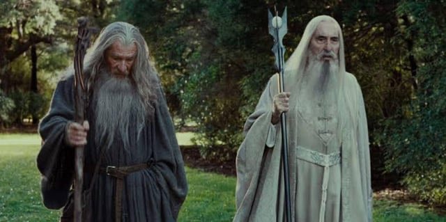 The caption does not match the image content, so any caption I produce risks reinforcing the post's false framing. 

That said, describing what is literally visible: two elderly bearded figures dressed in wizard-like robes stand on a grassy area with trees behind them, one holding a gnarled wooden staff and the other holding a more ornate staff. The image does not contain any NFTs, wallets, blockchain logos, tickers, or any verifiable on-screen text.

Would you like a caption that simply describes the scene as-is?