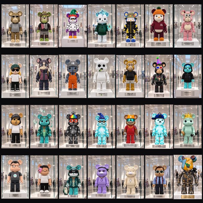 A 4x7 grid displays 28 unique BE@RBRICK-style bear figures displayed in glass cases, each reimagined as collectible art with distinct colors, outfits, and accessories reflecting different personalities. The image visually embodies the concept of transforming familiar PFP (profile picture) identities from social media timelines into stylized toy figures.