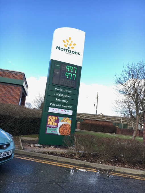 A Morrisons supermarket price totem displays diesel at 149.7 and petrol at 147.7, with service labels for Market Street, Halal Butcher, Pharmacy, and Cafe with Free WiFi, plus a 'Kids Eat Free' promotion.