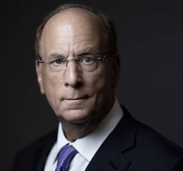 A formal studio portrait of a balding man wearing glasses, a dark suit, white shirt, and blue tie.