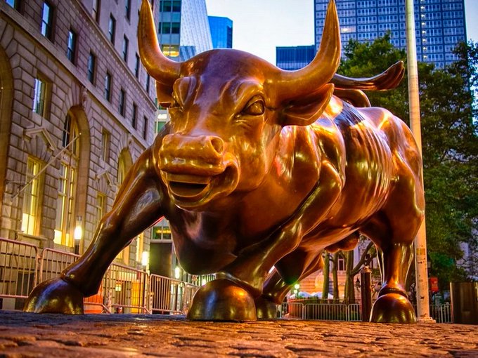 The bronze Charging Bull statue situated on a brick-paved street in New York City's financial district, photographed at dusk.