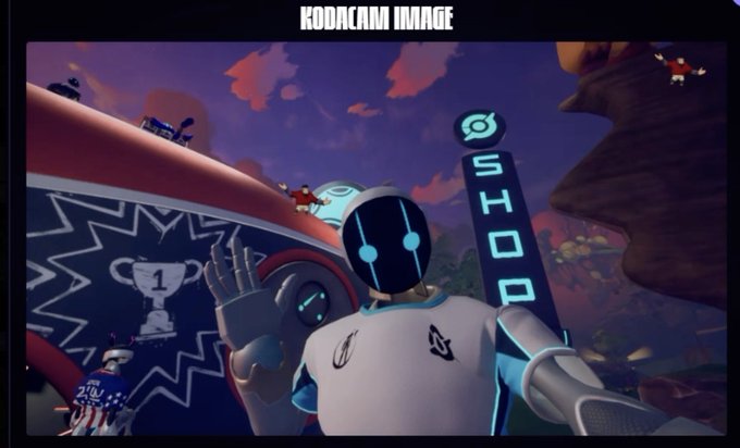 The image features a robot with blue eyes, wearing a white shirt that says "shoDACAM IMAGE". The robot appears to be waving or making a gesture towards the camera. In the background of the image, there are several people standing around in various positions, and a sign is visible as well.