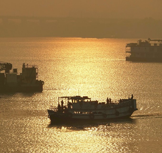 A golden sunset over a body of water, with silhouetted boats navigating the shimmering waves.
