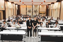 A large group of students poses for a photo in a lecture hall in Thailand during the Binance Academy University Tour, with attendees filling rows of desks while two individuals stand in the center holding a Binance-branded sign. The image captures the collaborative learning atmosphere as students engage with topics like Bitcoin's real-world value, risk and regulation, and institutional interest in crypto.