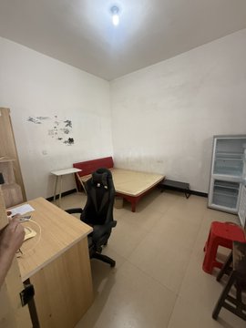 The image shows a sparsely furnished room with a simple bed, desk, and basic storage, reflecting the modest lifestyle mentioned in the post where the person, despite earning significantly, chooses to rent a simple 600 yuan room. The caption reads: "A person shares a simple, modestly furnished bedroom with a basic bed and desk, illustrating their choice to live frugally on a 600-yuan rental despite recently earning 300,000."