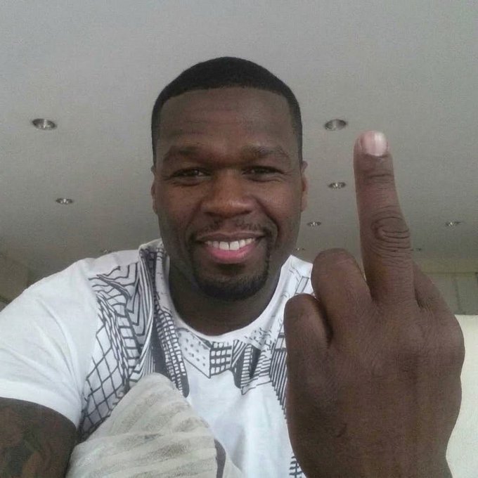 A smiling man takes a selfie while raising his middle finger toward the camera.