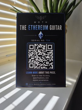A small black card or display titled 'THE ETHEREUM GUITAR' with 'MOTH' branding, showing 'SERIAL NO. 734', a QR code, and text indicating it links to more information about this piece.