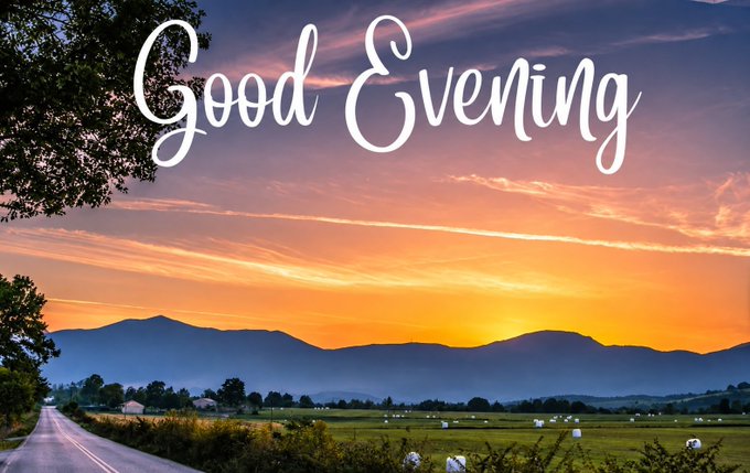A scenic landscape photograph showing a vibrant orange and pink sunset over silhouetted mountains with green fields and a road, overlaid with the white cursive text 'Good Evening'.