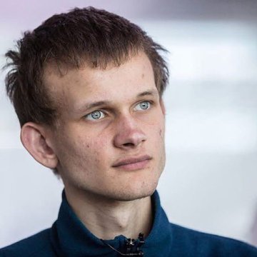 A portrait photograph of a young man with short brown hair and blue eyes wearing a dark blue zip-up jacket.