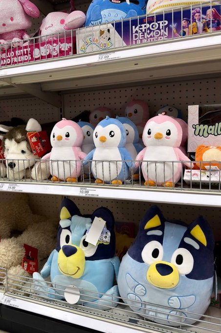 A retail display of plush toys featuring Bluey characters from the Australian children's show, with pink and blue penguins on the middle shelf and larger Bluey and Bingo plush toys on the bottom shelf priced at $10.99.