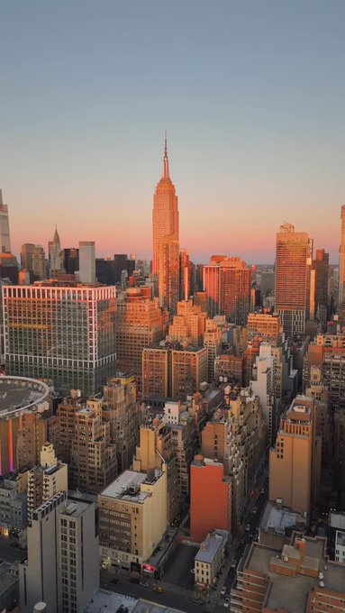 Aerial view of the New York City skyline at sunset, prominently featuring the Empire State Building bathed in golden light with surrounding Manhattan buildings.