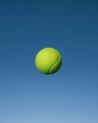 A yellow tennis ball suspended mid-air against a clear blue sky.
