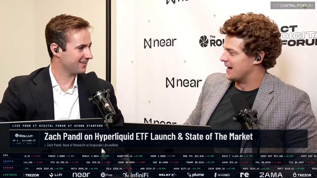The image shows two men talking at a conference with microphones behind them, against a green backdrop displaying text about Bitcoin,ETF, and the market. The main focus of the image appears to be the speakers, but the underlying message could potentially be related to cryptocurrency or investing in Bitcoin.