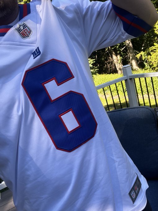A person wearing a white NFL jersey featuring the blue number 6 with red trim, standing outdoors on a deck.