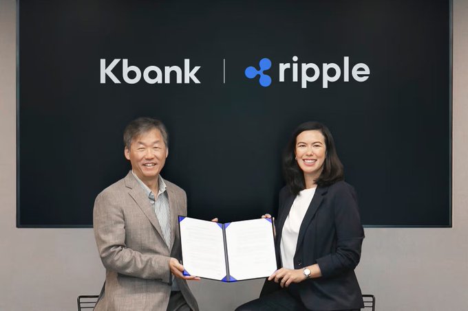Two executives smile as they hold open signed partnership documents beneath a "Kbank | ripple" banner, marking the formal agreement between Kasikornbank (Kbank) and Ripple to deploy institutional digital asset custody infrastructure.