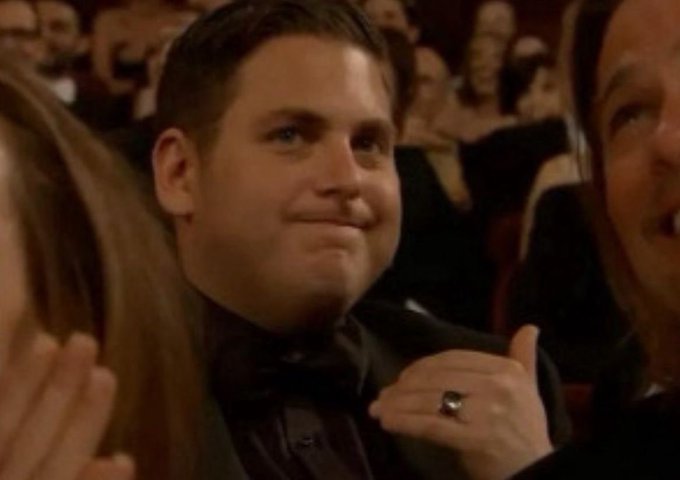 A close-up photo of a man in a tuxedo giving a thumbs up and smiling at what appears to be an awards show, wearing a large ring.