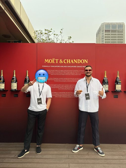 Two men pose in front of a Moët & Chandon Formula 1 Singapore Airlines Singapore Grand Prix display wall, holding champagne flutes—one making a peace sign while the other gives a thumbs up—capturing a luxurious moment from their F1 race day experience.