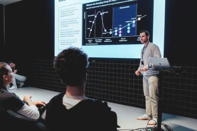A man presenting on stage in front of a projection screen displaying a graph titled 'Misses Are Emerging Along the Slope of Enlightenment' from the Gartner Hype Cycle, while an audience watches.
