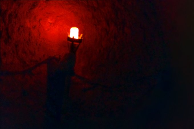 A glowing red light bulb illuminating a dark stone wall or tunnel, casting a moody red glow.