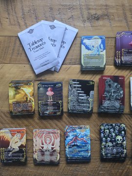 A collection of 'Talkoot Tarot' cards is arranged on a wooden table next to its guidebook, with some face-up cards including 'The Chariot' and 'IV'.