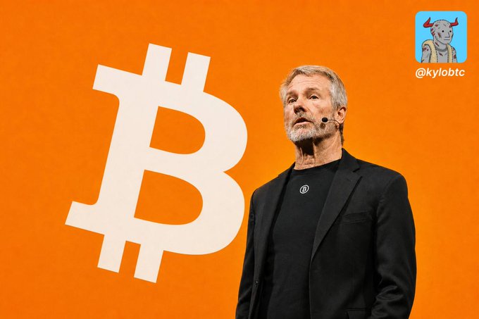A man in a black blazer speaks in front of a large Bitcoin logo on an orange background, with '@kylobtc' watermark.