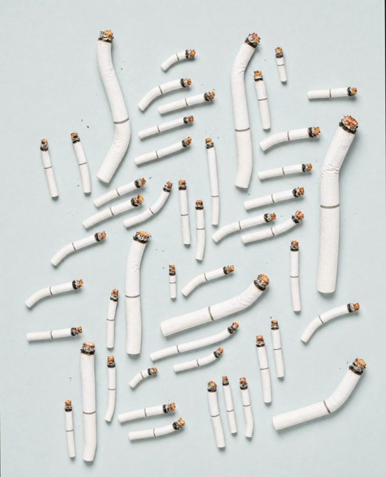 A scattered collection of handmade clay cigarettes with lit, burnt tips is arranged against a pale blue background, serving as a visual companion to a post promoting a quirky NFT collection by TomatoBird that humorously references the Virginia Slims 100s brand.