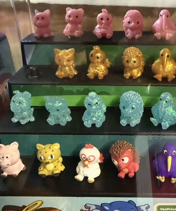 A display case showing four rows of small animal figurines, including pink, golden, glittery blue, and various colorful cartoon animal figures.