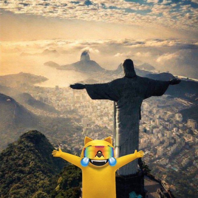 An aerial view of Rio de Janeiro's Christ the Redeemer statue with a cartoon emoji character (resembling a laughing-crying yellow cat with sunglasses) superimposed in the foreground with arms outstretched.