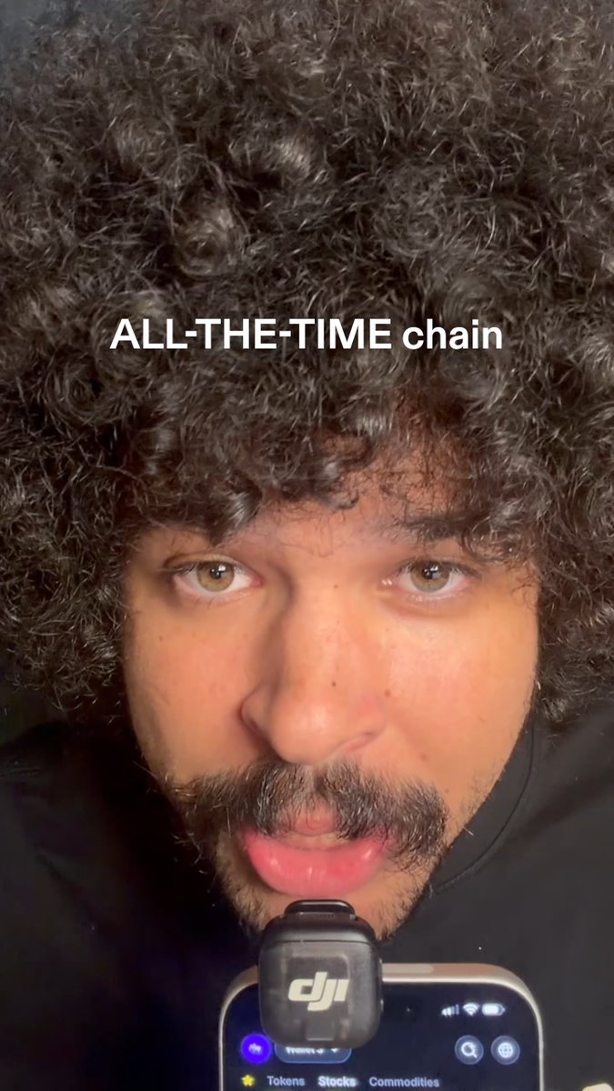 A close-up selfie shows a man with a curly afro and mustache holding a phone displaying the DJI Mic receiver, with the text "ALL-THE-TIME chain" overlaid at the top—visually playing on the "24/7, 365 days a year" theme by suggesting stock trading on Solana never sleeps.