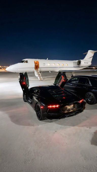 A nighttime shot featuring a black Lamborghini Huracán with scissor doors open parked on a snowy tarmac, with a private jet and an SUV in the background.
