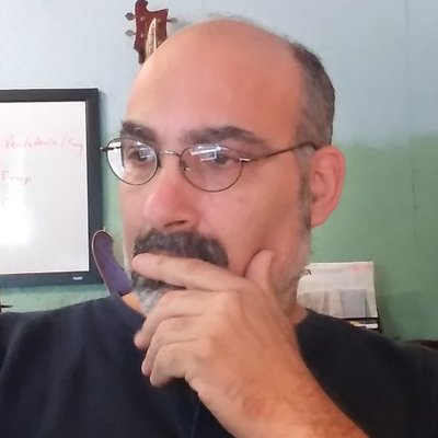 A bald man with glasses and a beard holds a smoking pipe thoughtfully to his chin, appearing contemplative as he discusses Bitcoin and the failures of fiat currency.