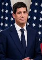 A heavily motion-blurred image showing a person in a dark suit with a white shirt against a background that appears to be an American flag.