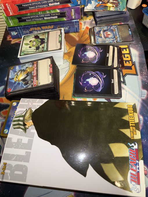 A collection of Beyblade X trading cards, trial decks, and starter sets from Palworld and Star Wars are spread across a table, with a large Beyblade X "Soar Dragon T Tre'ekombo" card prominently displayed in the foreground. The "GN X" caption likely refers to "Beyblade X" (the brand), matching the Beyblade-themed merchandise shown throughout the image.