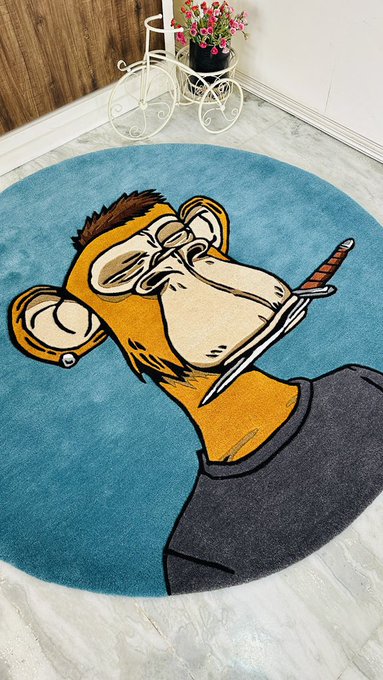 The image features a unique, hand-made blue circular rug with an illustration of a monkey holding a sword. The monkey appears to be wearing a black shirt and has a pair of glasses on its face. The rug is placed on a white floor next to a white bicycle parked against the wall. There are also two potted plants in the room - one near the left side and another towards the right side, adding some greenery to space.