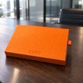 A bright orange Hermès box sitting on a dark wooden surface, likely packaging for a luxury accessory.