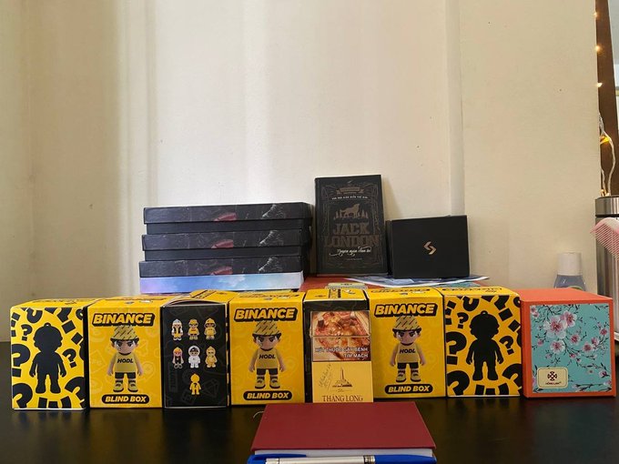 A collection of "Binance HODL" blind boxes, alongside other mystery boxes, including one with Jack London text, are displayed on a table. These items visually represent the "blind box" concept mentioned in the accompanying post.