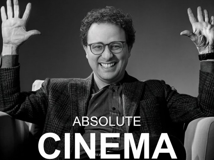 A black and white promotional image featuring a smiling man with glasses raising his hands enthusiastically, with the text 'ABSOLUTE CINEMA' displayed prominently at the bottom.