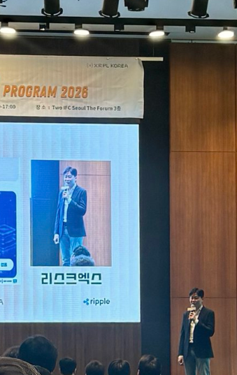 A presenter speaks on stage at "KFIP 2026" sponsored by Ripple, with a screen showing "PROGRAM 2026," "XRPL KOREA," and Korean text alongside a photo labeled "리오크엠오" (Lee Ock-mo), capturing the moment SIVAX won first place in the XRPL Korea competition.