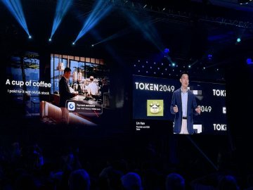 A man presents on stage at TOKEN2049 Singapore, with a large screen behind him reading 'A cup of coffee - I paid for it with coffee sound' alongside the TOKEN2049 branding.