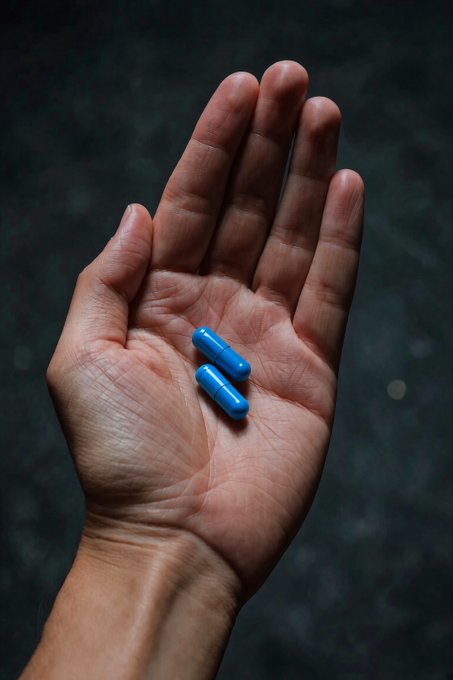 A hand holds two blue capsules against a dark backdrop, visually reinforcing the caption's metaphor about taking one's "daily dose" of @base.