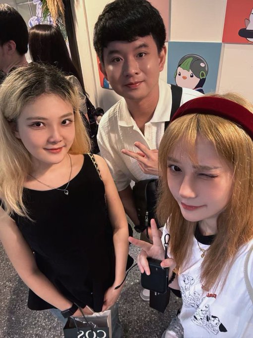 Three young people pose for a selfie, with a man in the center making a peace sign between two women, one winking at the camera.
