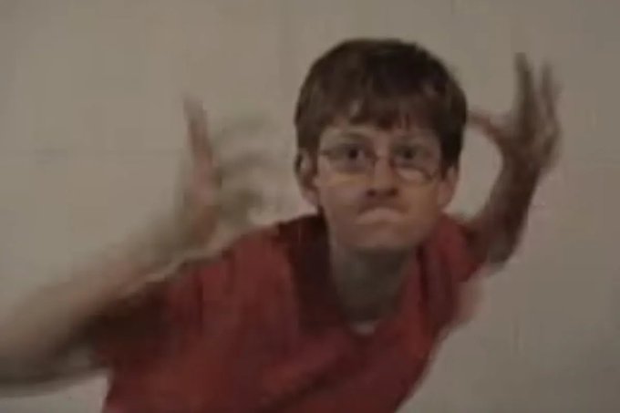 A blurry meme image showing a person with glasses and a red shirt making an exaggerated claw-like gesture with both hands raised near their face.