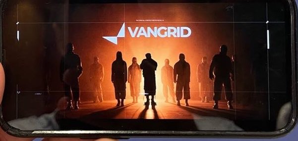 A smartphone screen displaying the 'VANGRID' logo with silhouettes of people standing against a dramatic orange-lit background.