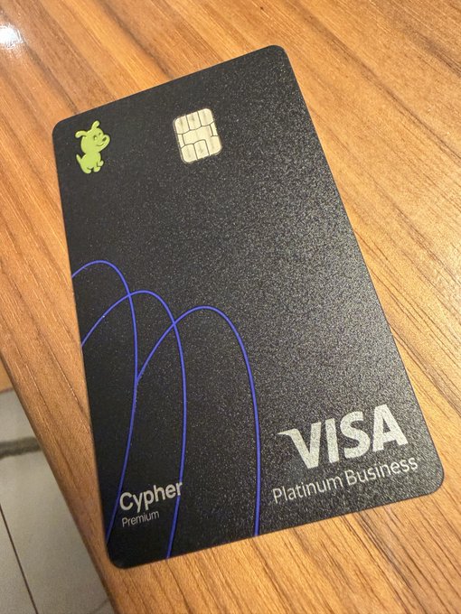 A black metal Cypher Premium Visa Platinum Business card rests on a wooden surface, featuring a small green crocodile logo and blue curved line designs. The image illustrates the writer's frustration with their Cypher crypto debit card experience, specifically highlighting the metal card they purchased to use in supporting the Base chain.