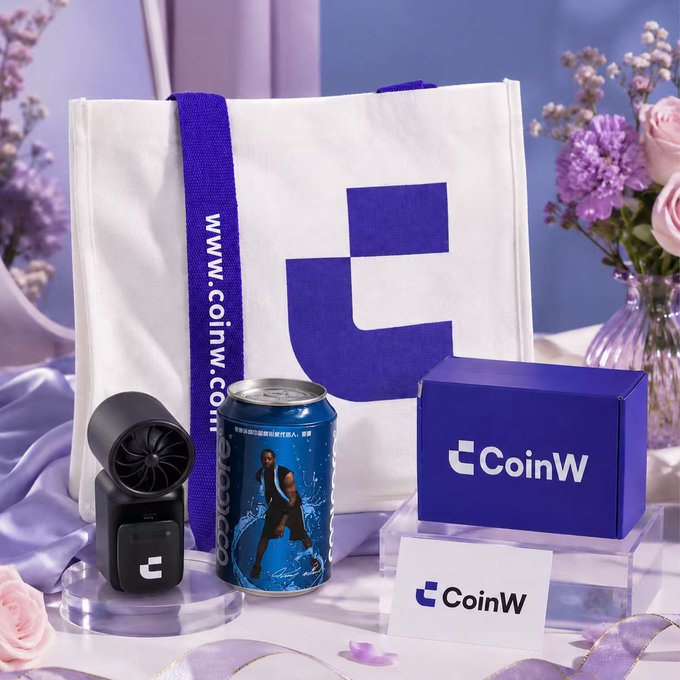 A promotional product photo for CoinW cryptocurrency exchange featuring a white tote bag with blue logo, a branded can with a basketball player, a small fan, and a blue gift box arranged with flowers.