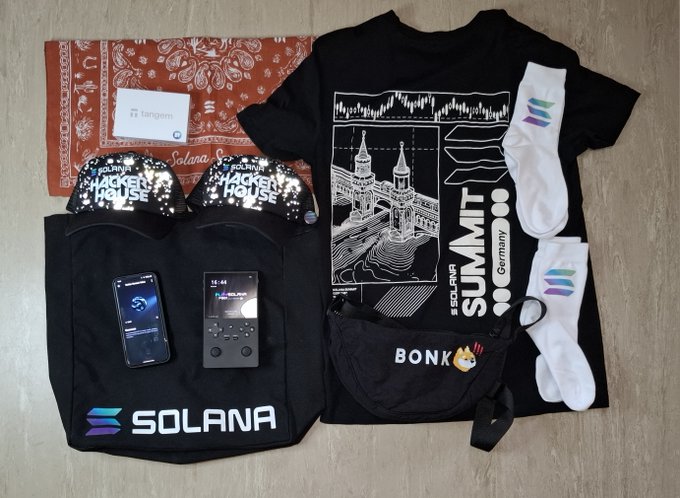 Flat lay of Solana-branded swag including a Solana t-shirt, Soneium socks, Hacker House sunglasses, Tangem card, MP3 player, smartphone, fan, and bandana from what appears to be a Solana Summit Germany event.