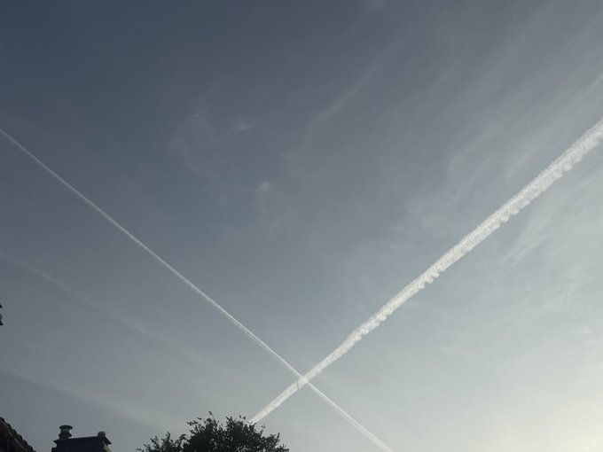 The image features a large, white contrail or jet stream that appears to be coming from the top left corner of the frame. This contrail is located above an area with houses visible in the background. The photo has been captioned with the phrase "When you see your favorite app in the sky".