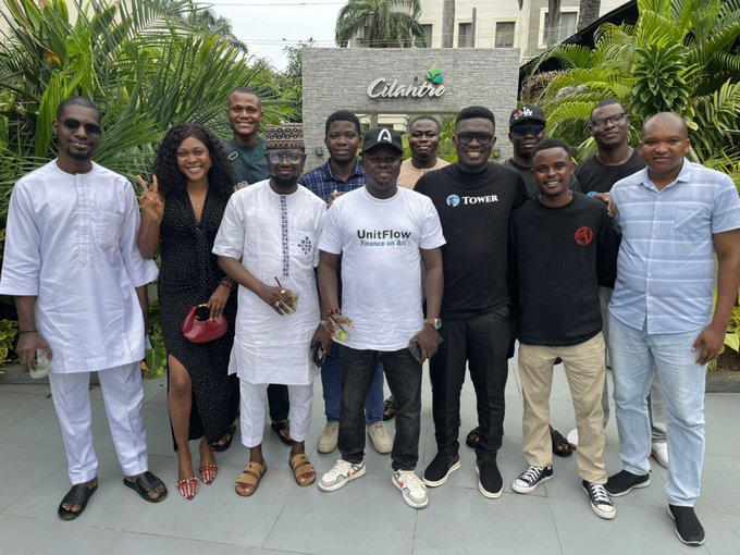 A diverse group of approximately eleven people pose together outdoors in front of a building displaying a "Cilantro" sign, with one individual wearing a "UnitFlow" shirt. The gathering appears to celebrate the Arc Mainnet launch on 9.16.26, with team members dressed in a mix of casual and traditional attire, reflecting the collaborative spirit behind the project.