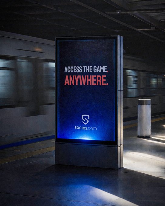 A glowing digital advertising kiosk stands in a dim subway station displaying "ACCESS THE GAME. ANYWHERE." for Socios.com, its dark blue illuminated panel cutting through the underground ambiance to reinforce the campaign's tagline about staying connected to one's club anytime, anywhere.
